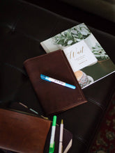 Load image into Gallery viewer, Brown leather notebook with markers on a dark surface

