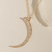 Load image into Gallery viewer, Gold crescent moon necklace with small stones on a beige background
