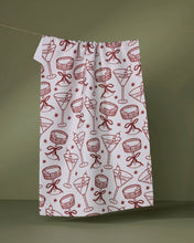 Load image into Gallery viewer, Fabric with red cocktail and bow pattern on a white background, hanging against a green wall.
