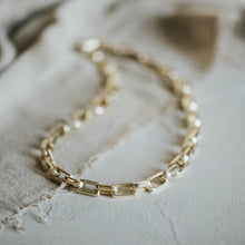 Load image into Gallery viewer, Gold chain necklace on a textured beige fabric background

