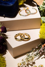 Load image into Gallery viewer, Gold hoop earrings on a white box with flowers around
