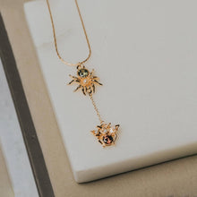 Load image into Gallery viewer, A delicate gold lariat-style necklace featuring a spider and a small butterfly pendant, styled on a light beige stone slab.
