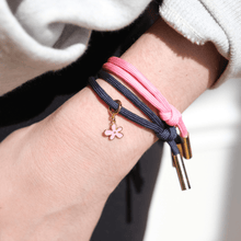 Load image into Gallery viewer, Close-up of a wrist wearing two braided bracelets with floral charms on a neutral background
