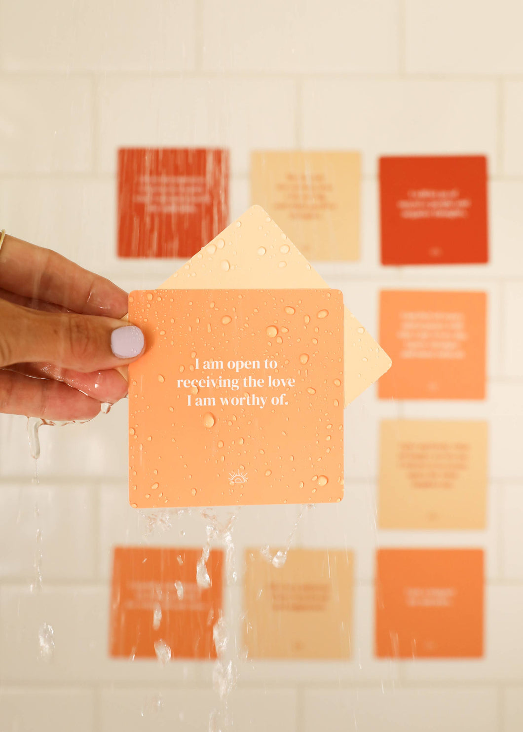 Hand holding a motivational card with affirmations on a tiled wall background