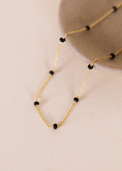 Gold necklace with black beads on a beige background