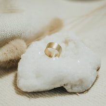 Load image into Gallery viewer, Gold ring on a white stone with a soft focus background
