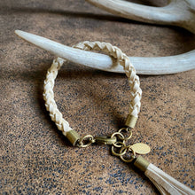 Load image into Gallery viewer, Bracelet with braided design and tassel on a textured surface with antlers in the background
