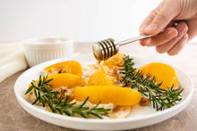 Load image into Gallery viewer, Honey being drizzled over a dish with yellow vegetables and herbs on a white plate.
