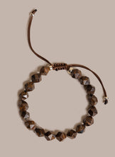 Load image into Gallery viewer, A beaded bracelet with faceted brown beads and a brown adjustable cord, displayed on a solid beige background.
