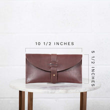 Load image into Gallery viewer, Brown leather clutch bag on a marble table with measurements indicated.
