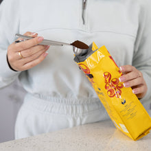 Load image into Gallery viewer, Person measuring coffee from a yellow package using a spoon.
