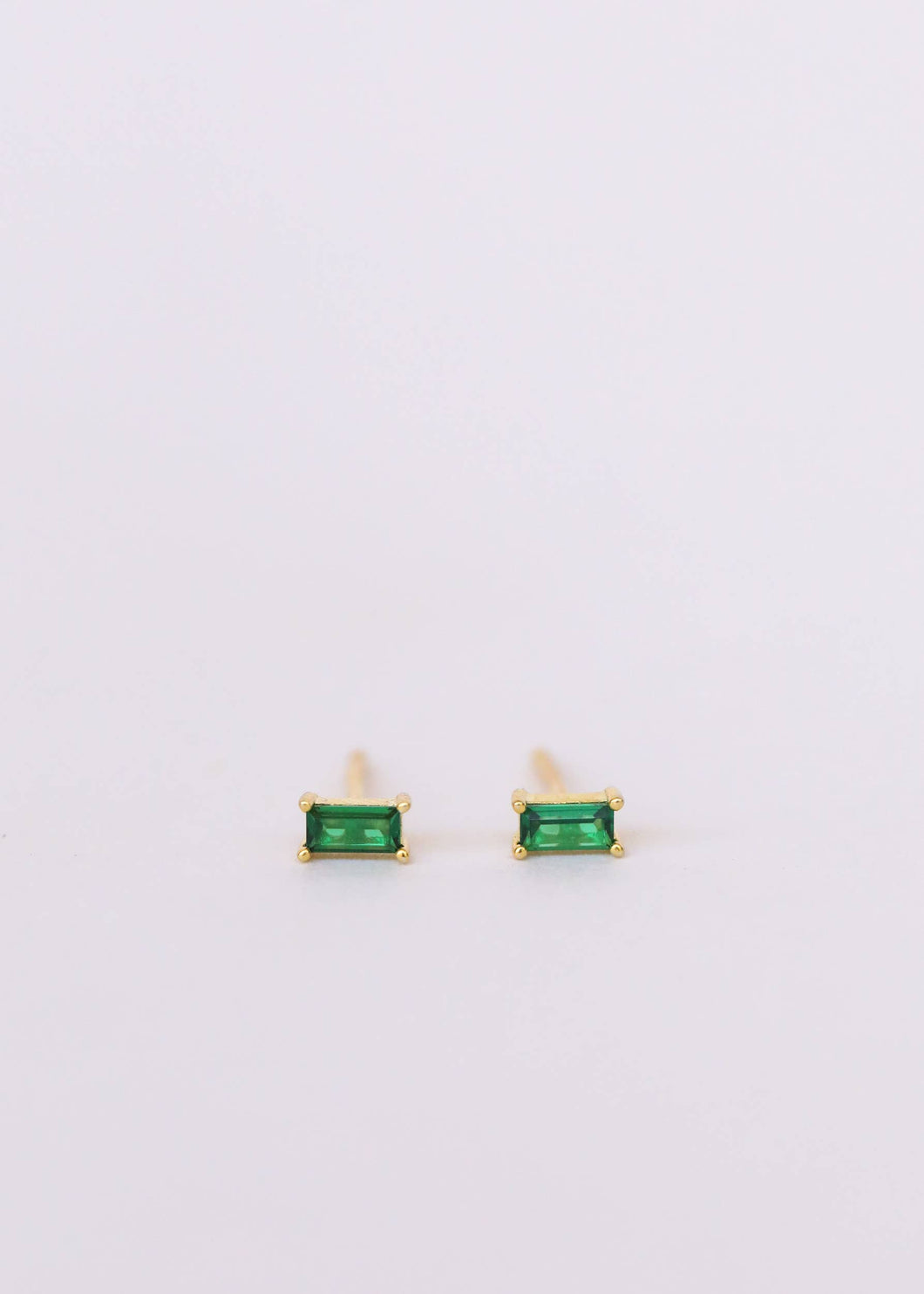 A pair of emerald green baguette-cut stud earrings on a white background